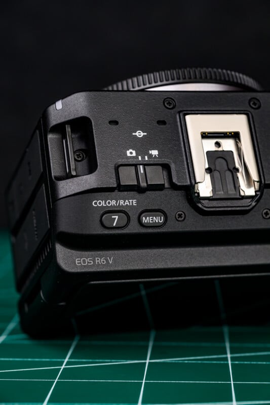 Close-up of the top section of a Canon EOS R6 V camera, showing buttons labeled "COLOR/RATE 7" and "MENU," with a hot shoe mount and part of a green cutting mat in the background.