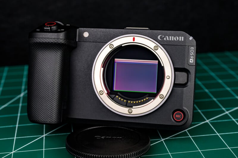 A Canon EOS R camera body without a lens, showing its sensor, sits on a green cutting mat with the lens cap placed in front of it.