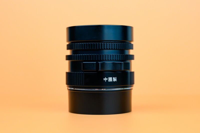 A black camera lens with Chinese characters on it is standing upright against a solid orange background.