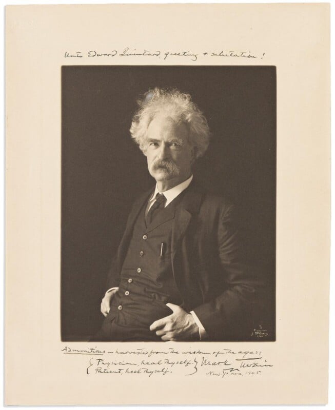 A sepia-toned portrait of an older man with white hair and mustache, wearing a dark suit and vest, seated with one hand in his pocket. Handwritten notes and a signature appear above and below the photograph.