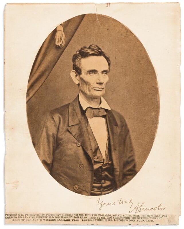 A sepia-toned portrait of Abraham Lincoln with a serious expression, wearing a bow tie and suit, shown inside an oval frame. The bottom of the image includes his signature and a typed caption.