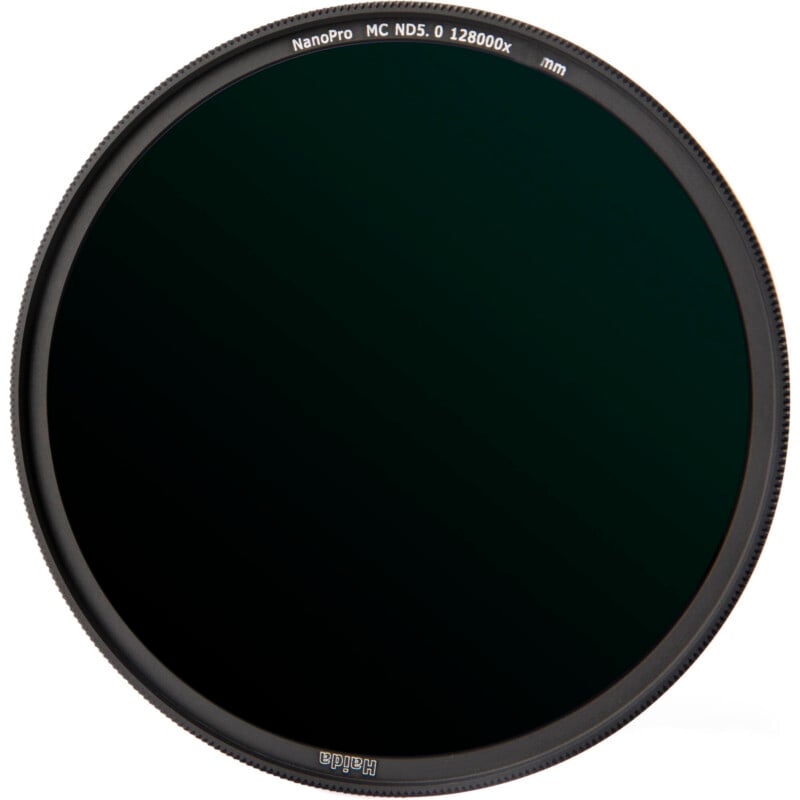 A circular dark neutral density camera lens filter with a thin black frame, labeled "NanoPro MC ND5.0 128000x" along the edge. The filter appears nearly opaque with a subtle greenish tint.