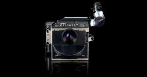 A high-end IMAX KEIGHLEY film camera is displayed against a black background, featuring a large central lens, carbon fiber texture, and an attached viewfinder on the top right.
