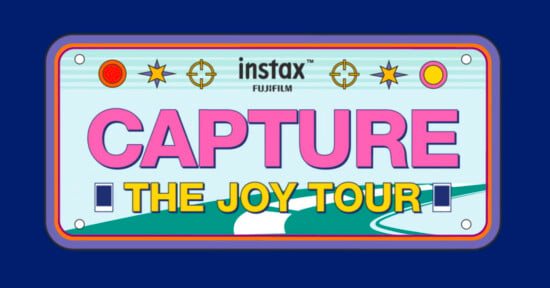 A colorful sign styled like a license plate reads "instax FUJIFILM CAPTURE THE JOY TOUR" with stars, circles, and a winding road graphic against a blue background.