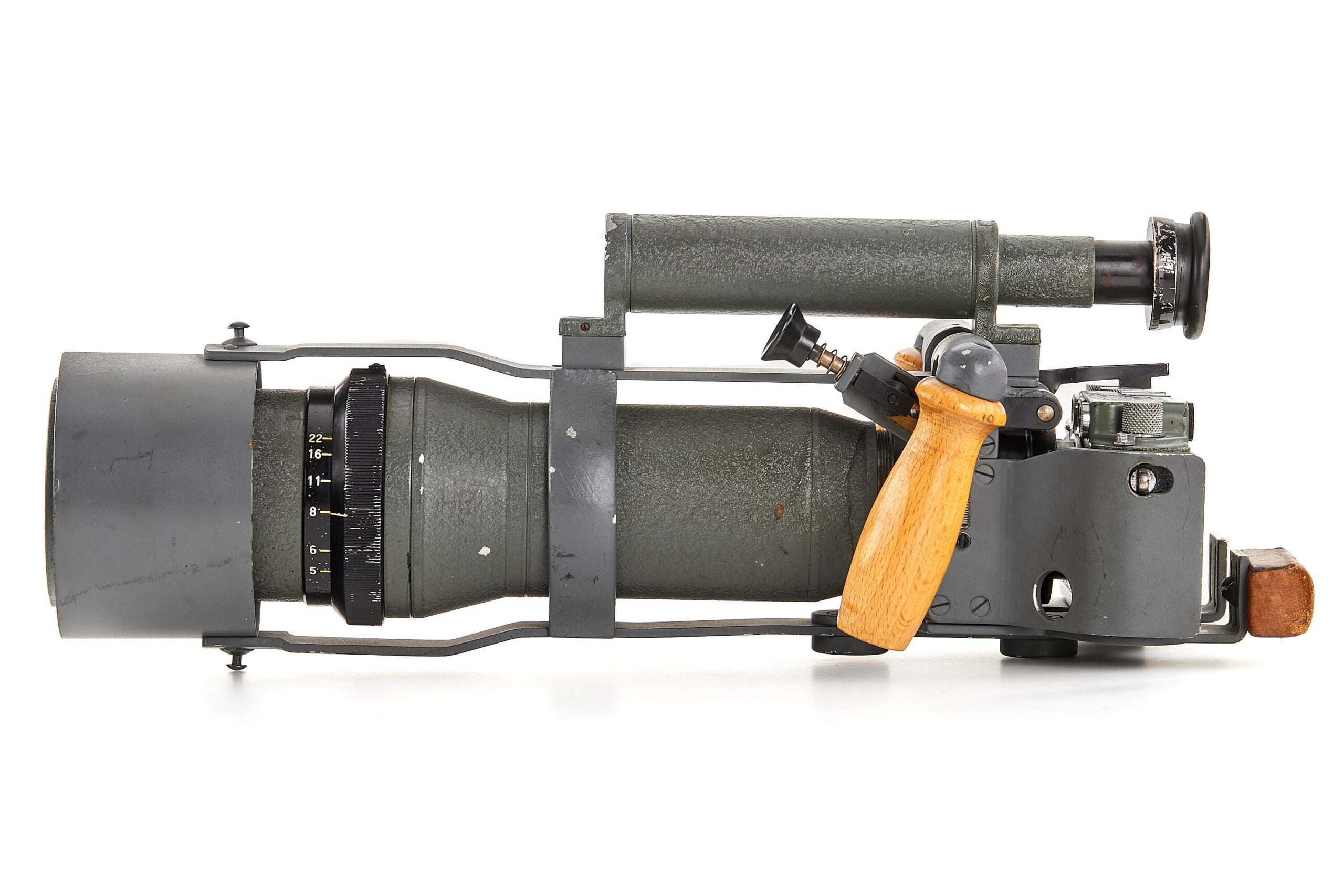 A military-style optical device with a large lens, adjustment dials, a wooden handle, and an attached eyepiece, all in a metallic gray-green housing. The device appears rugged and utilitarian.