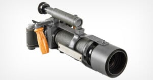 A vintage camera with a long telephoto lens, wooden grip, and metal body, featuring an eyepiece and viewfinder, set against a plain white background.