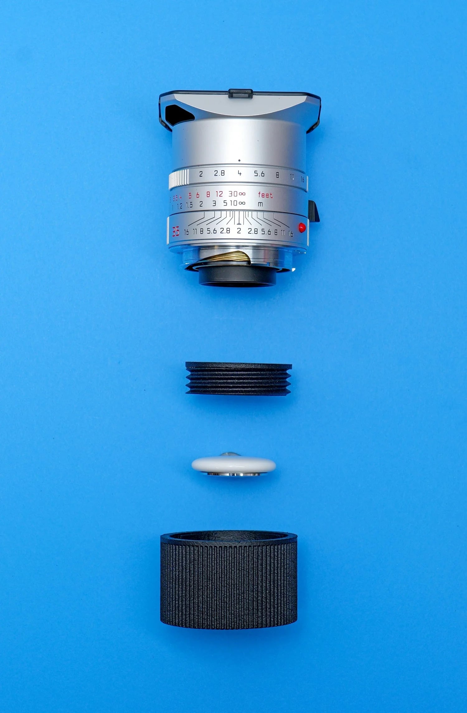 A camera lens and its components, including a lens cap and mounting ring, are arranged vertically in an exploded view against a bright blue background.