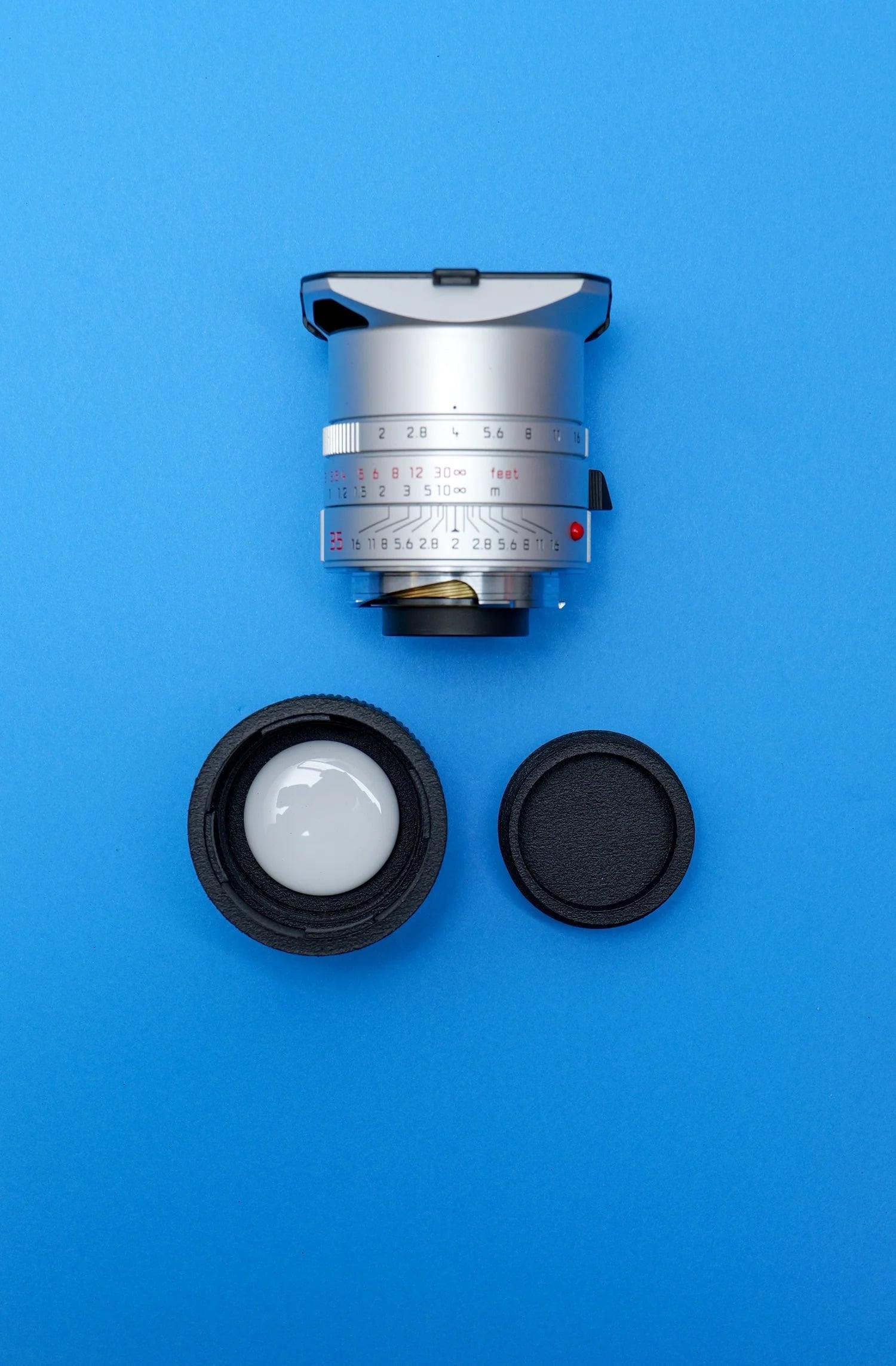 A silver camera lens with focus markings is placed above two black lens caps on a solid blue background.