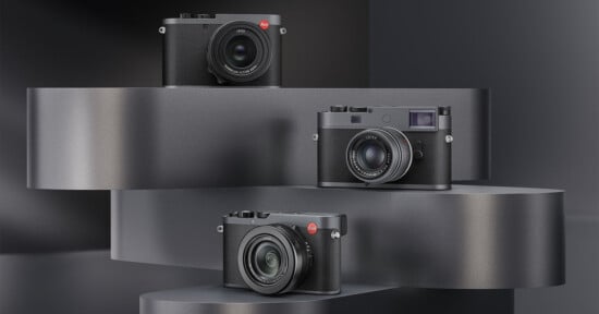Three black Leica cameras with red logos are displayed on staggered, curved metallic platforms against a dark, modern background.