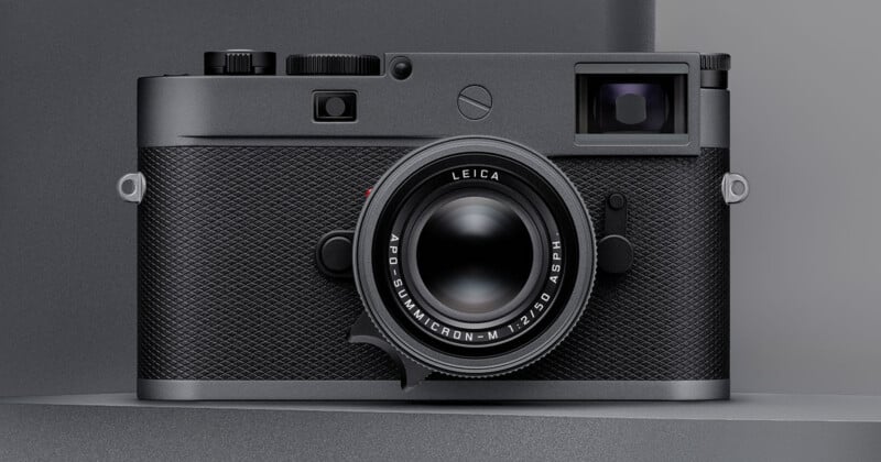 A close-up view of a black Leica camera with a textured body and prominent lens, displayed against a neutral gray background.