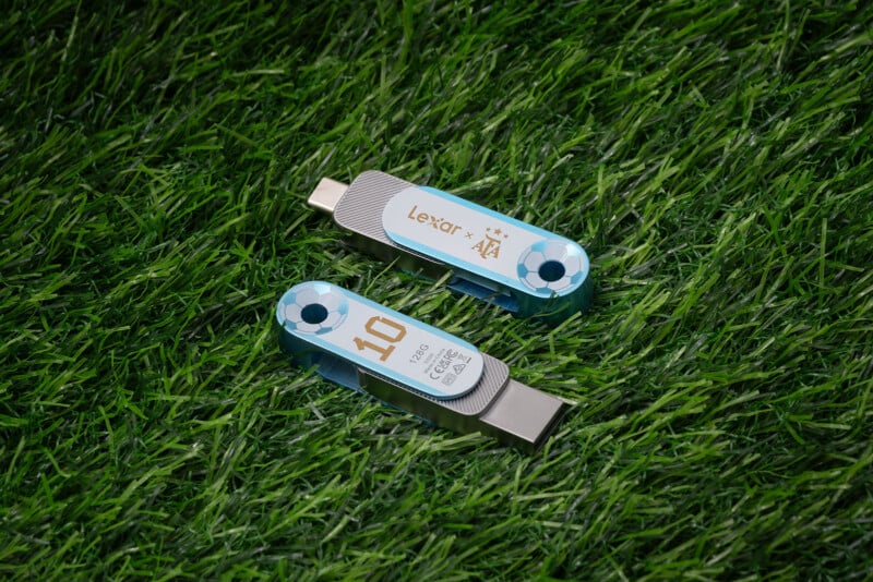 Two Lexar USB flash drives with light blue accents, placed on green grass. One drive is labeled "10" and "512GB," with its USB connector exposed, while the other is closed and displays the Lexar and AFA logos.