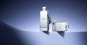 Two silver Lexar USB flash drives are displayed on a smooth, curved surface with a blue gradient background; one drive is standing upright with its connector exposed, while the other is lying horizontally.