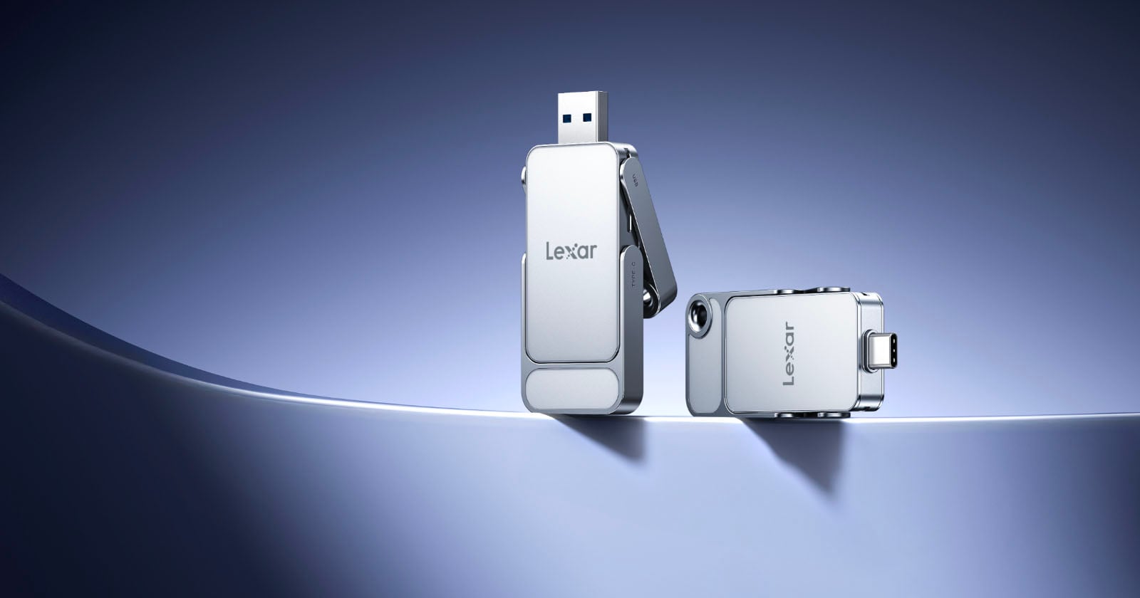 Two silver Lexar USB flash drives are displayed on a smooth, curved surface with a blue gradient background; one drive is standing upright with its connector exposed, while the other is lying horizontally.