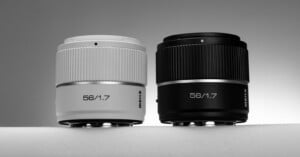 Two camera lenses are displayed side by side against a neutral background, one in white and the other in black. Both lenses have "56/1.7" prominently printed on the front.