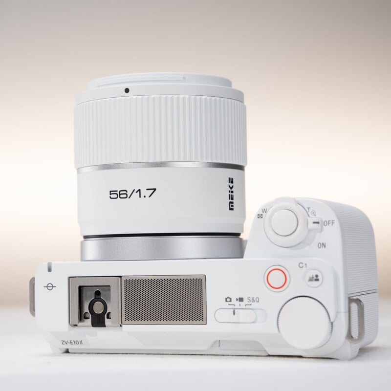 A white digital camera with a white Meike 56mm f/1.7 lens, shown from above against a light background, highlighting the camera controls, dials, and lens details.