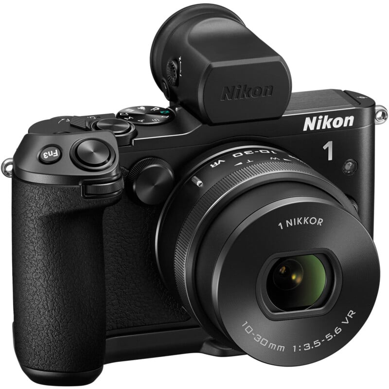 A black Nikon digital camera with a 1 NIKKOR 10-30mm lens, textured grip, electronic viewfinder, and various control buttons, shown on a white background.
