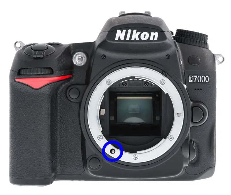 Front view of a Nikon D7000 DSLR camera body without a lens, showing the lens mount and a small metal sensor contact circled in blue.