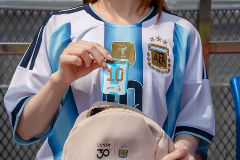 A person wearing an Argentina soccer jersey holds a keychain with the number 10 above a beige backpack. The Argentina Football Association (AFA) logo and stars are visible on the jersey and the backpack.