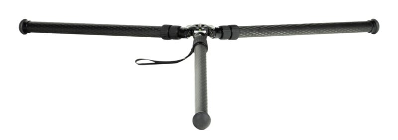 A tripod viewed from above with two legs extended horizontally to the sides and one leg pointing downward; the tripod is made of carbon fiber with rubber grips and a wrist strap attached.