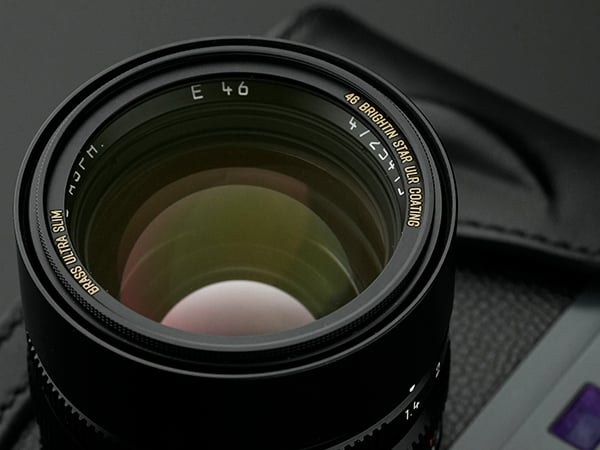 Close-up of a camera lens with "E 46" and "4D Brightn Star Ultra Coating" written on the rim, placed on a dark, textured surface.