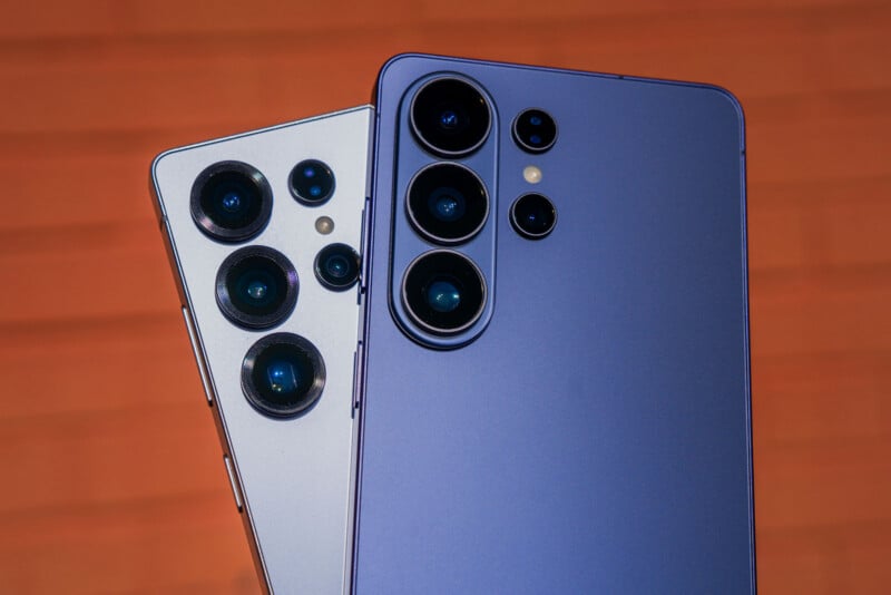 Close-up of the rear cameras on two modern smartphones, one silver and one purple, both featuring multiple camera lenses, set against a blurred orange background.