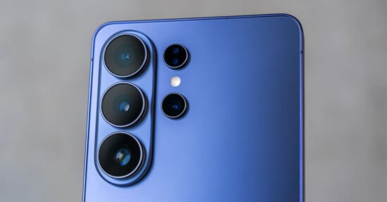 Close-up of the rear camera module of a blue smartphone with four camera lenses and a flash, set against a blurred gray background.