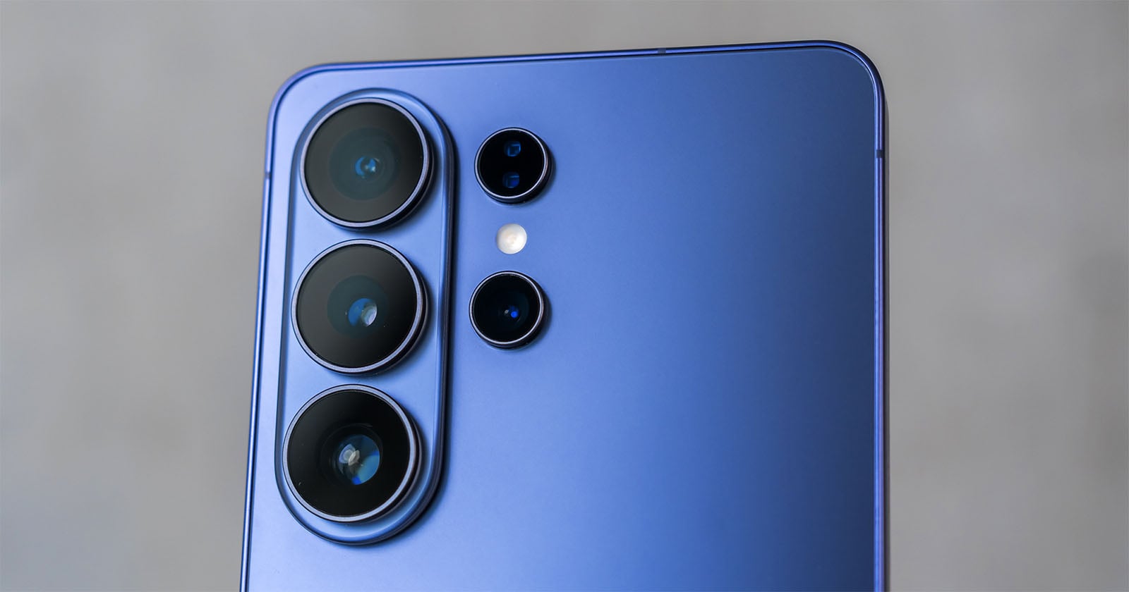 Close-up of the rear camera module of a blue smartphone with four camera lenses and a flash, set against a blurred gray background.