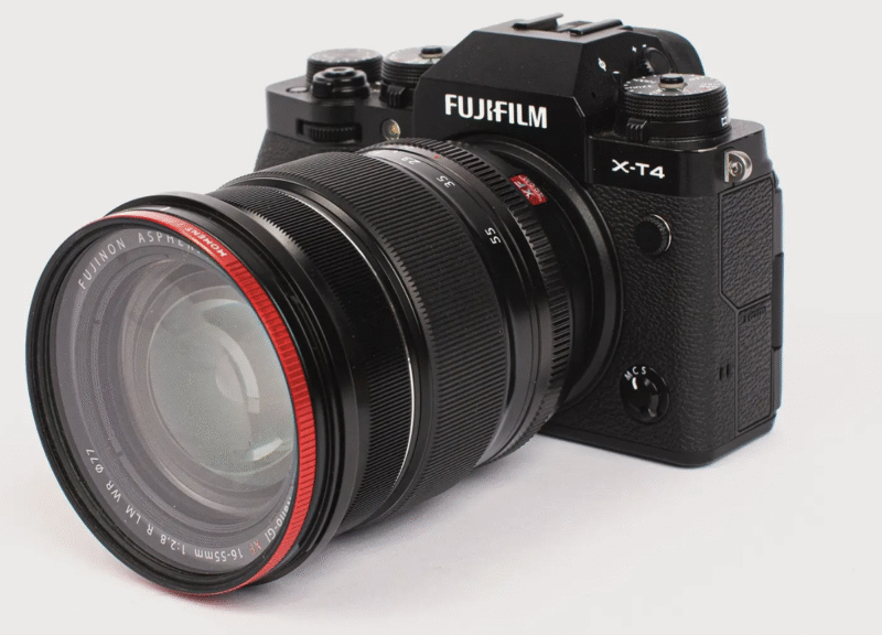 A black Fujifilm X-T4 mirrorless digital camera with a large zoom lens featuring a red ring near the front, shown on a white background.