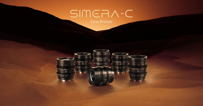 Six camera lenses are arranged on a smooth, sandy surface with a warm, orange-brown gradient background. "SIMERA-C Cine Primes" is written above the lenses in white text.