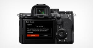 The back of a digital camera displays its screen showing a firmware update prompt, with options to "Execute" or "Cancel" and a message about the update process and automatic reboot.