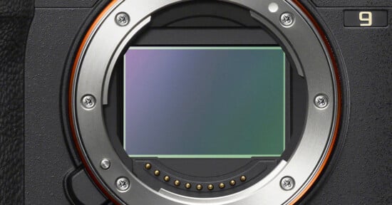 Close-up view of a digital camera's exposed sensor and metal lens mount, showing electronic contacts and screws, with part of the camera body visible on the left and a number "9" on the top right.