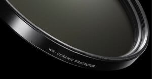 Close-up view of a camera lens filter labeled "WR-CERAMIC PROTECTOR" against a black background, showing the detailed edge and smooth glass surface.