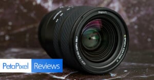 A close-up of a camera lens with visible reflections, lying on a dark marbled surface. The image includes a "PetaPixel Reviews" banner in the lower left corner.