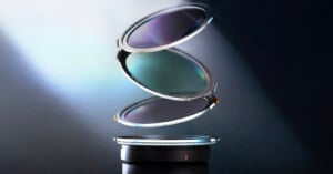 Three circular camera lens filters are floating above a camera lens in a vertical stack, separated and illuminated by a beam of light against a dark background.