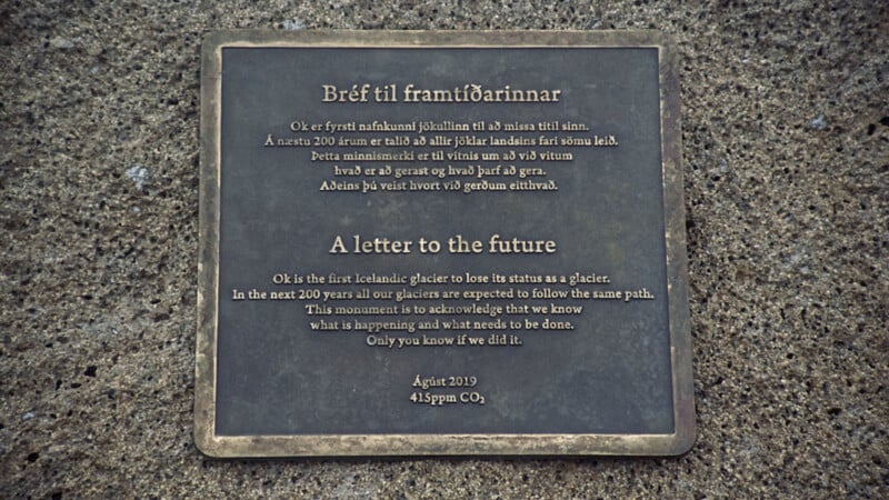 A bronze plaque on stone displays text in Icelandic and English, commemorating the Ok glacier lost to climate change in August 2019. It serves as a letter to the future, warning of glacier loss and urging climate action.