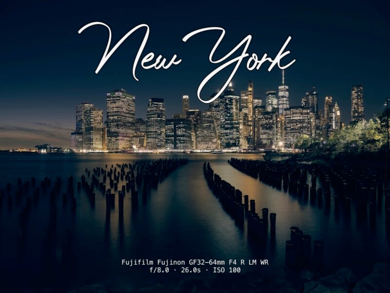 Nighttime view of the New York City skyline with illuminated skyscrapers, wooden posts in the water, and "New York" written in large script across the top. Camera settings are listed at the bottom.