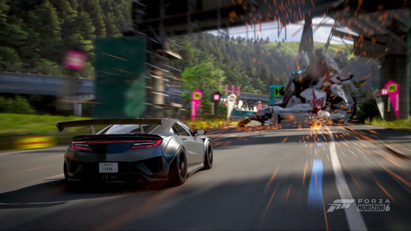 A sleek sports car speeds down a road as a large robot crashes, spraying sparks, against a scenic backdrop of trees and mountains in the video game Forza Horizon 6.