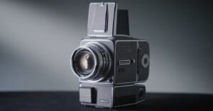 A vintage medium format camera with a large lens and waist-level viewfinder sits on a dark surface against a softly lit background.