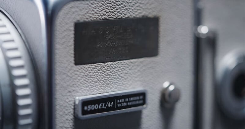 Close-up of a vintage Hasselblad camera showing textured metal surface, a blurred engraved label, and a clear “500EL/M” model badge with “Made in Sweden” visible. Buttons and part of the lens are also in view.
