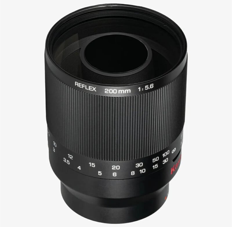 A black 200mm f/5.6 camera lens with REFLEX branding, featuring a ribbed focus ring and marked distance scale, shown against a light gray background.