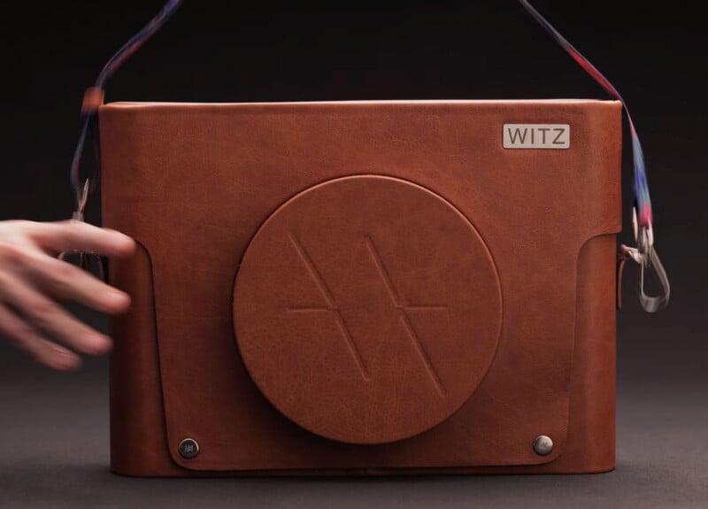 A brown leather bag with a round embossed design and the word "WITZ" on a metal plate. A hand is reaching toward the bag, which has a multicolored strap and silver hardware accents.