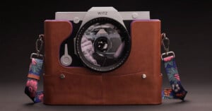 A modern camera with the brand name "Witz" is partially enclosed in a brown leather case with floral-patterned straps, set against a dark background. The camera lens reflects an image of hands holding a camera.