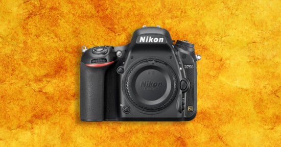 A Nikon D750 DSLR camera body is centered on a textured, orange-yellow background. The camera’s lens mount is visible, and the Nikon logo is clearly displayed at the top.