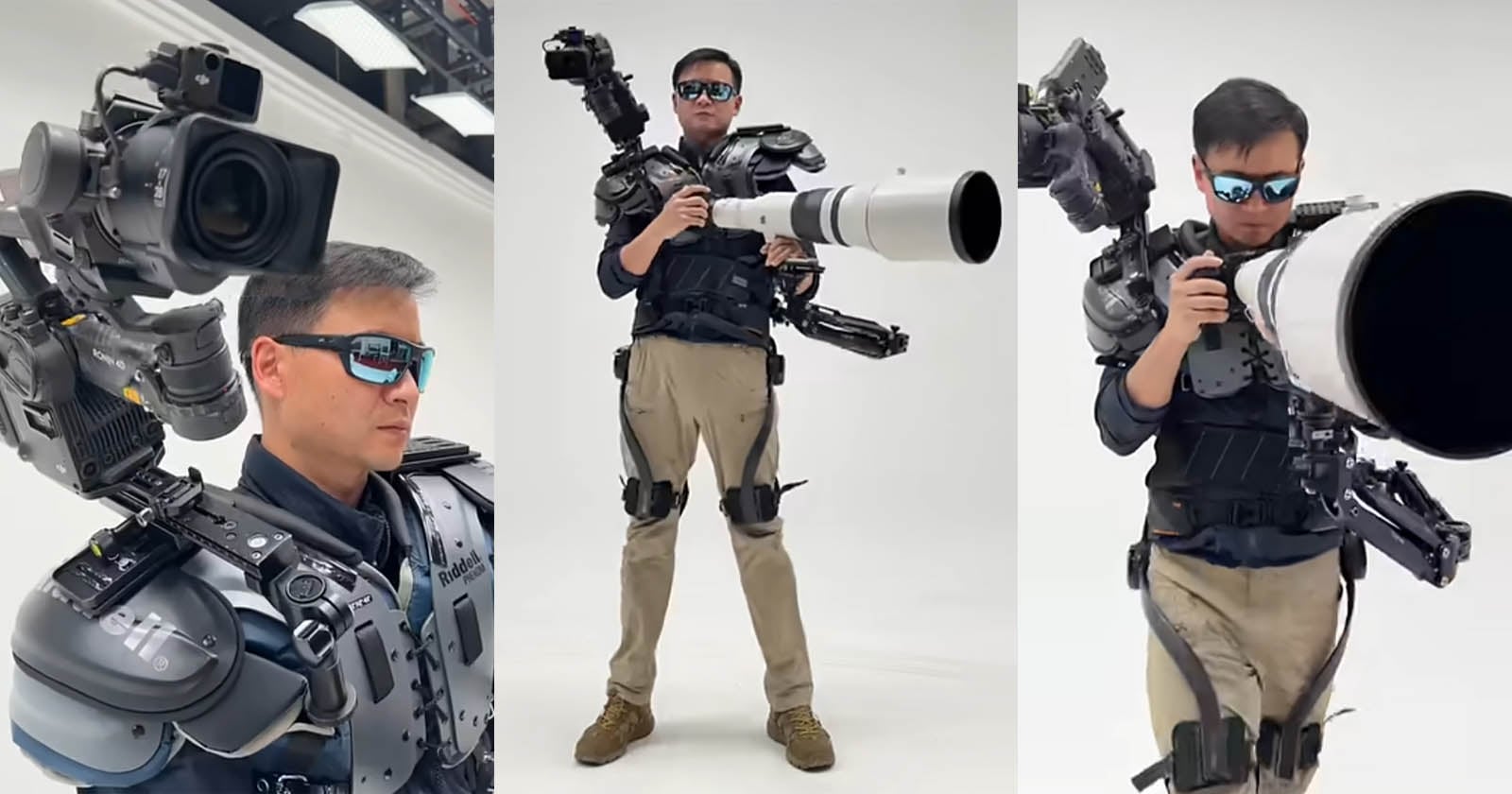 A man wearing sunglasses and a futuristic black and gray exoskeleton suit holds and operates a large camera with an oversized telephoto lens in a white studio setting. The suit has mounted camera gear on his shoulders.