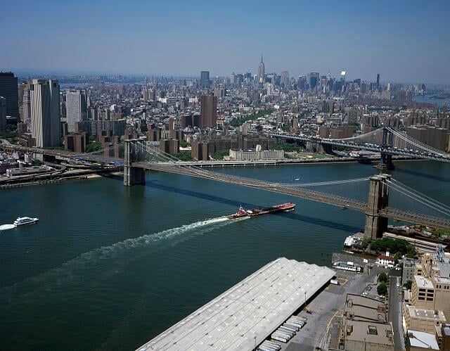 Aerial view of New York City showing the Brooklyn and Manhattan Bridges crossing the East River, with the city skyline and skyscrapers visible in the background on a clear day.