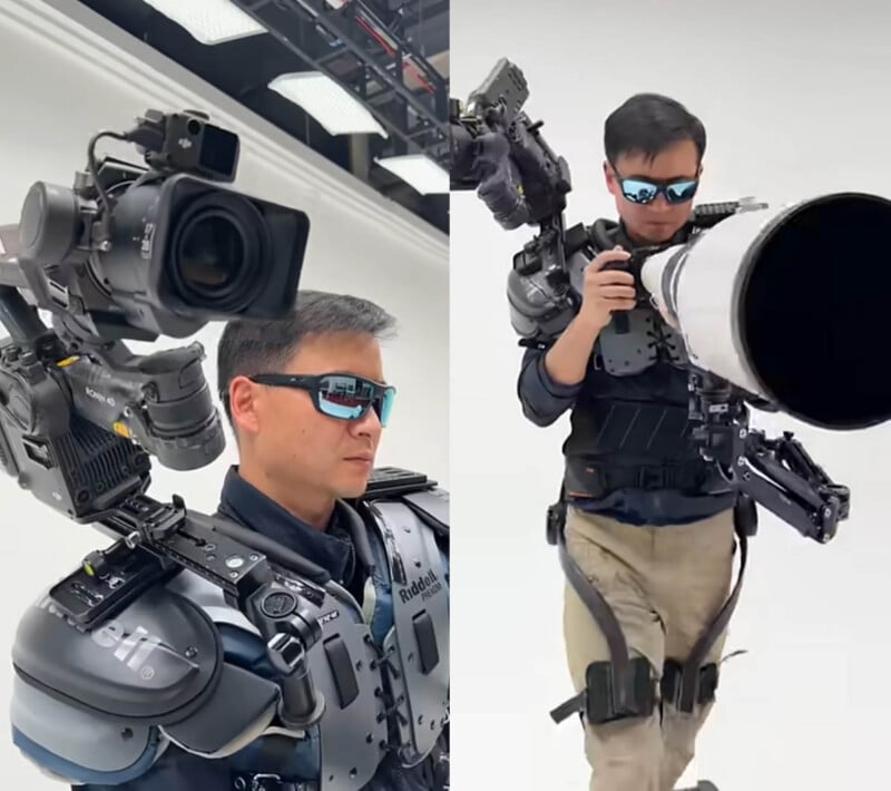 A man wearing sunglasses and a futuristic exoskeleton suit operates a large professional camera setup, with various camera equipment mounted on his shoulders and arms. The background is a white studio.