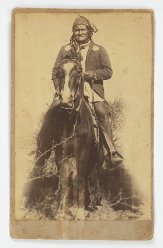 A sepia-toned, vintage photograph of an Indigenous man wearing a headscarf and jacket, sitting on a horse, looking toward the camera. The photo shows signs of age, with visible creases and marks.