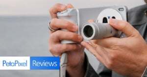 A person holding and using a silver camera with both hands near a body of water. The image features the "PetaPixel Reviews" logo in the bottom left corner.