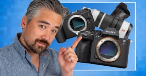 A man with gray hair and a beard points at two mirrorless cameras, a Canon and a Sony, set against a blue, pixelated background.