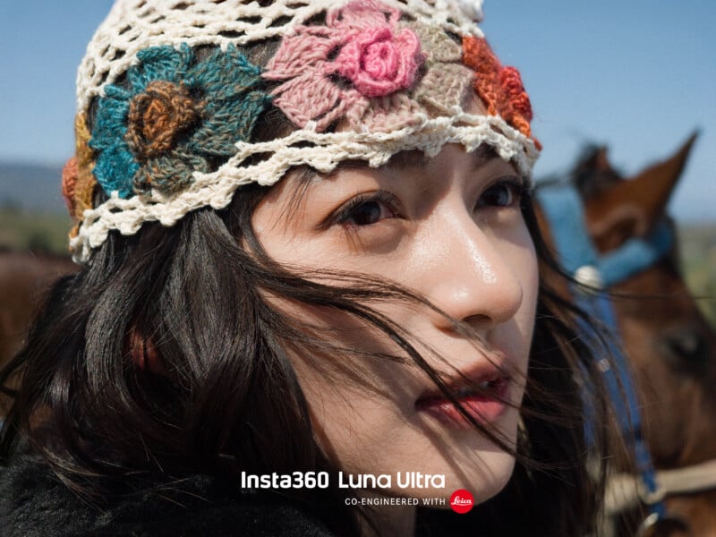 Close-up of a young woman with dark hair, wearing a crocheted hat decorated with colorful flowers. She is outdoors with a blurred horse and blue sky in the background. Text at the bottom reads, "Insta360 Luna Ultra CO-ENGINEERED WITH Leica.